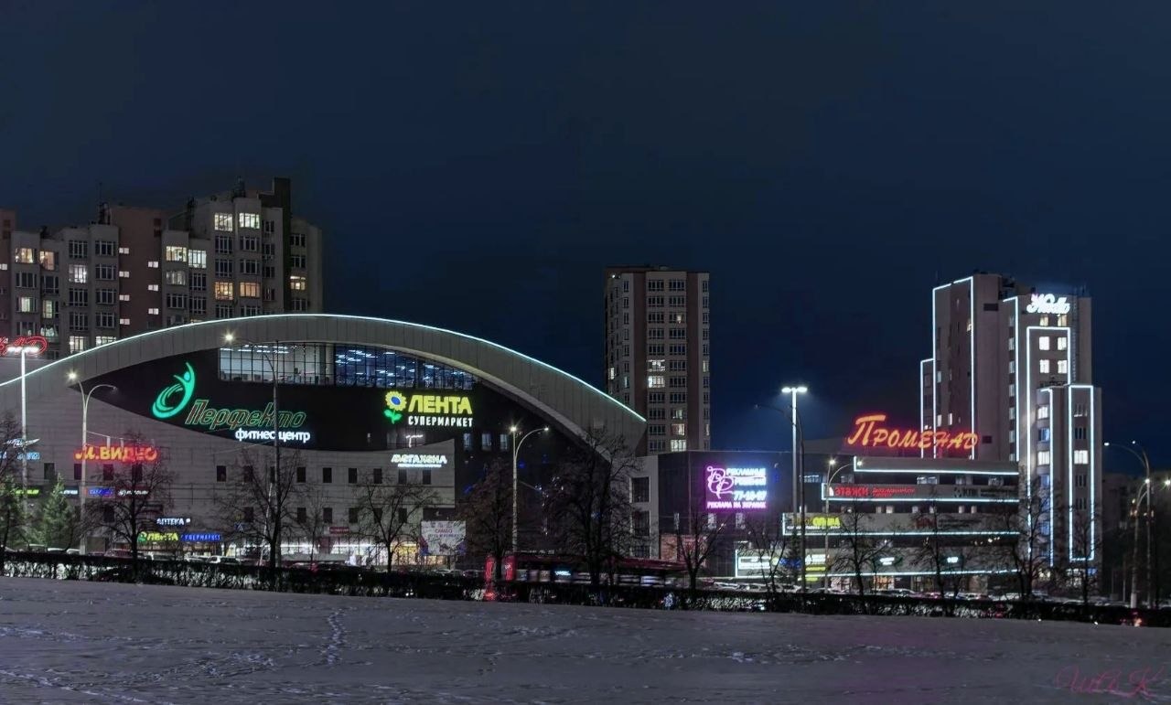 Городские здания и яркие вывески торгового центра в вечернем свете.