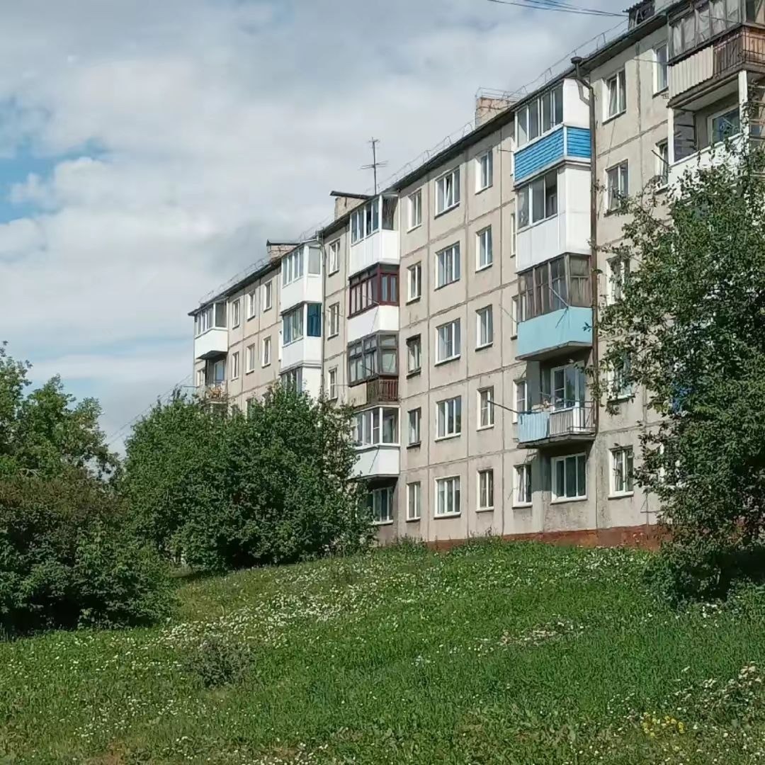 Жилой дом рядом с зелёным склоном и дворовой дорожкой.