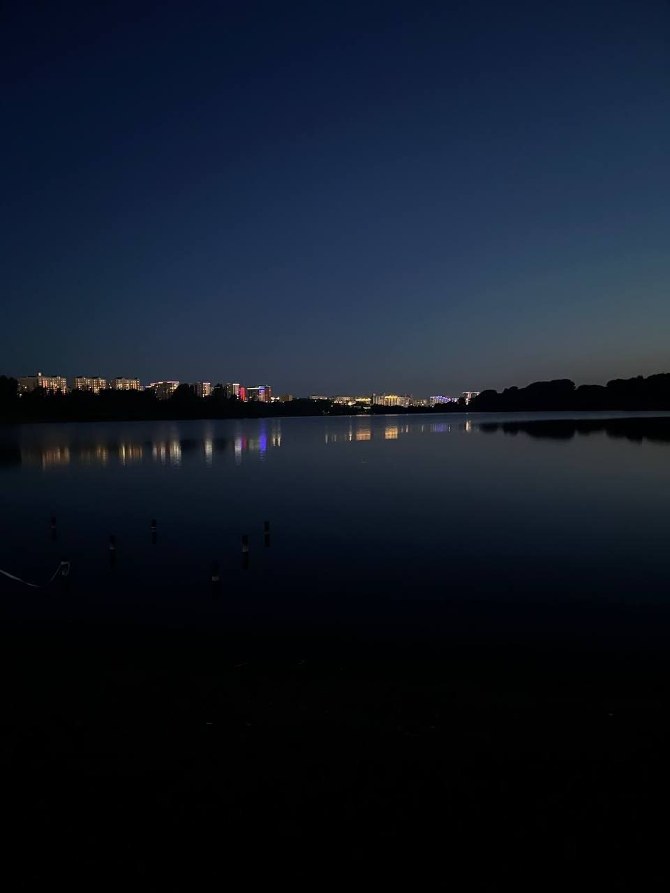 Дальние городские огни отражаются в тёмной воде озера.